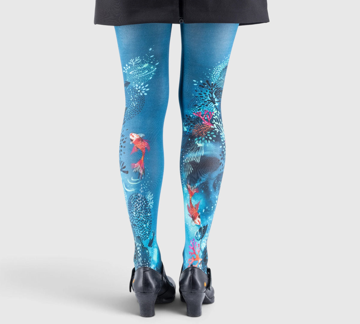 Jambes d’une personne portant des collants bleus à impressions coralliennes et poissons, vue de dos.