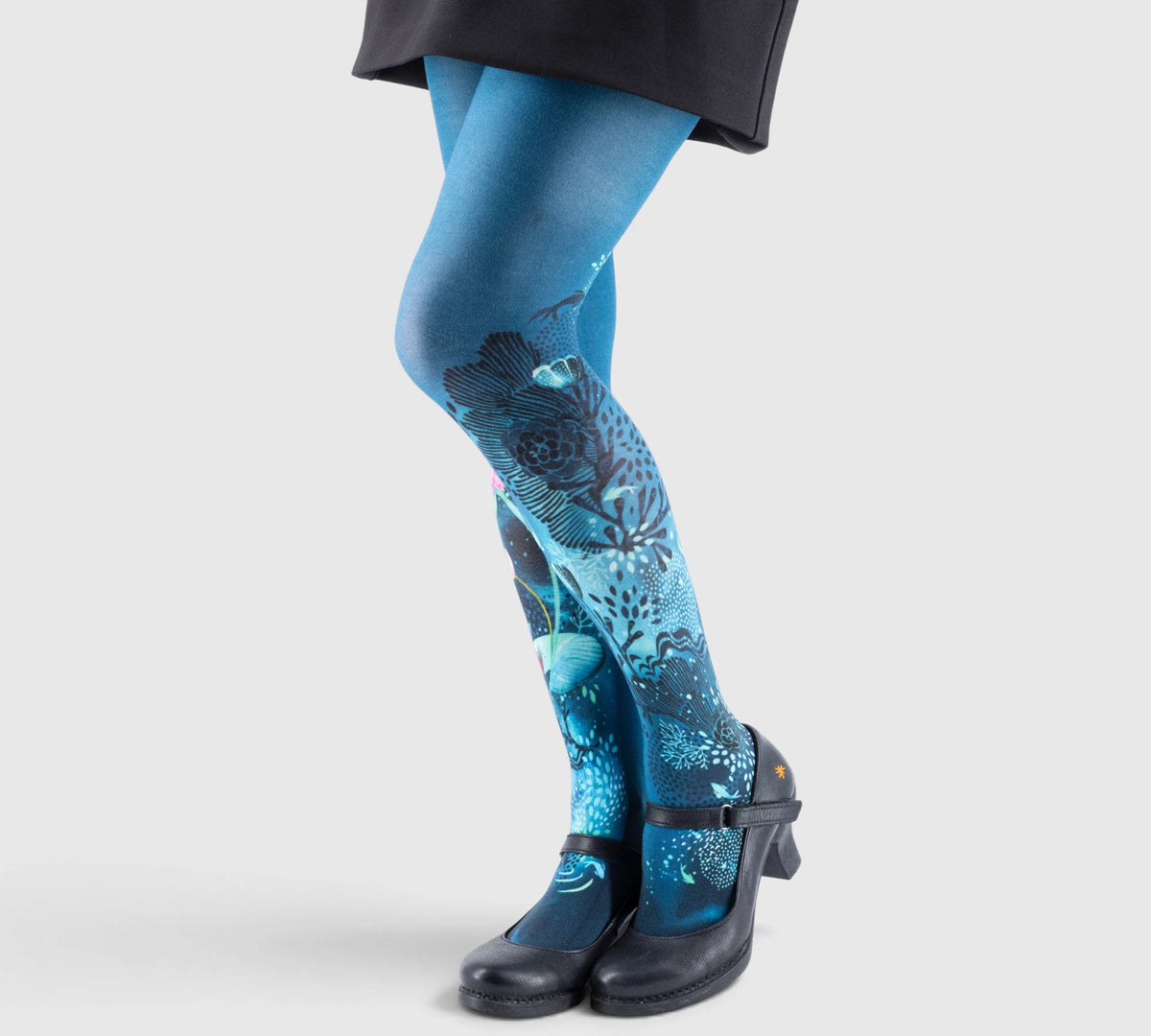 Jambes d’une personne portant des collants bleus imprimés motifs floraux, avec chaussures noires à petit talon.