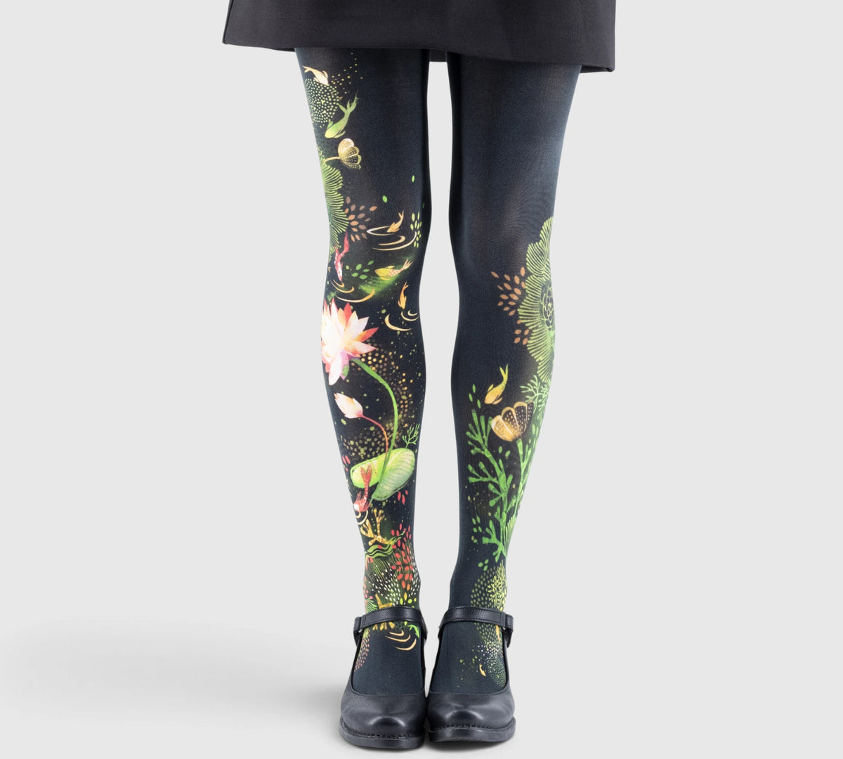 Jambes d'une enfant portant des collants imprimés floraux et herbes aquatiques, chaussures noires à bride.